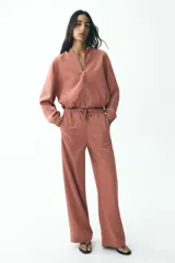 Chaqueta corta color rosa con capucha y manga larga terminada en puño. Tiene bolsillos de vivo en el delantero, bajo ajustable con cordones elásticos y cierre frontal con cremallera.