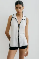 Blusa color beige con cuello camisero y botones frontales, sin mangas y con ribete negro en cuello, sisas y ruedo.