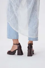 Sandalias de cuero negro con plataforma y tacón cuadrado alto. Presentan una tira delgada sobre los dedos y pulsera tobillera con hebilla dorada.