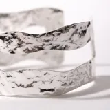 Brazalete plateado con diseño texturizado y forma ondulada.