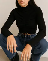 Sweater negro de lanilla con cuello alto y mangas largas. Presenta un frunce central con cordones ajustables.