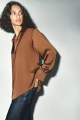 Camisa azul marino de satén, con cuello solapa, escote en pico y mangas largas con puños abotonados. Cierre frontal con botones.