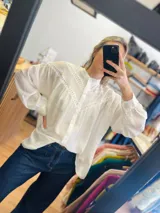 Camisa blanca oversize con detalles de puntilla en el frente y mangas abullonadas.