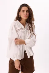 Blusa blanca amplia con detalle de bordados y puntillas, escote en V con lazo y mangas largas con elástico.