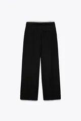 Pantalón negro de tiro alto con doble cintura elástica ajustable con cordón y tejido combinado. Pinzas frontales, bolsillos delanteros y falso bolsillo de vivo en espalda. Pernera ancha.