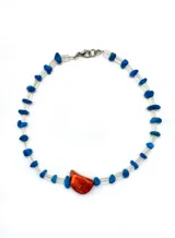 Collar hecho a mano con cuentas azules y una piedra roja central, con terminaciones en acero quirúrgico.