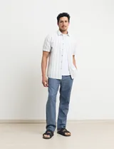 Camisa de manga corta a rayas verticales celestes y blancas, con cuello clásico y botones marrones.