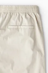 Pantalón color beige de popelina de algodón, corte ancho, con cintura elástica ajustable con cordón, bolsillos laterales y traseros.