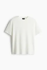 Remera blanca de punto texturizado de peso medio, corte estándar, cuello redondo y mangas cortas.