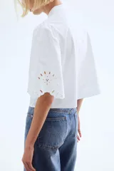 Blusa blanca de algodón con cuello mao y botones. Manga abullonada al codo con broderie tono sobre tono y puños festoneados.