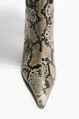 Botas altas de caña recta con estampado de piel de serpiente en tonos beige, marrón y negro. Poseen punta fina y taco aguja bajo.