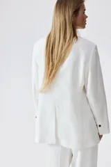 Blazer blanco de lino con solapas de pico, hombreras finas y cierre de un botón. Modelo entallado con pinzas en la cintura, abertura con botón en los puños y bolsillos delanteros ribeteados. Abertura atrás y forro interno.