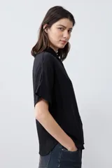 Camisa negra de manga corta con cuello clásico y cierre frontal con botones.