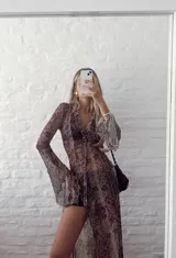 Vestido largo de gasa transparente con estampado de piel de serpiente en tonos marrones. Tiene cuello camisero, mangas largas acampanadas y abertura frontal con cordones.