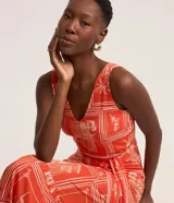 Vestido midi sin mangas confeccionado en viscosa estampada con motivos geométricos y florales en tonos naranja y blanco. Presenta escote en V, corte a la cintura con lazo y falda con volantes.