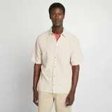 Camisa de manga corta color beige claro, con cuello clásico y cierre frontal con botones. Confeccionada en mezcla de lino.