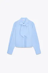 Camisa celeste de cuello redondo y manga larga, con lazo en el delantero y cierre frontal con botones.