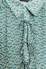 Camisa de manga larga con estampado floral en tonos verde y azul. Tiene cuello solapa, cierre frontal con botones y lazadas en los puños.