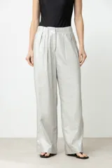 Pantalón de tiro alto, color plateado metalizado, con pliegues frontales y corte ancho y largo.