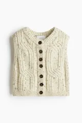 Chaleco corto de punto grueso color crema con textura tweed (neps oscuros), diseño sin mangas y escote en V con cierre frontal de botones marrones.