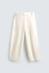 Pantalón color crema de corte ancho, con pliegues frontales, bolsillos laterales y traseros.