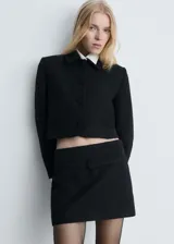 Chaqueta corta de tweed negro con cuello camisero, cierre frontal con botones y dos bolsillos laterales.