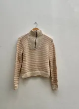 Suéter tejido a mano en 100% lana merino, color crudo, con cuello alto y cierre metálico.