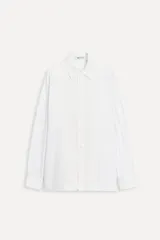 Camisa blanca de popelina de algodón con corte recto, cuello solapa, manga larga con puños abotonados, cierre frontal con botones y detalle de panel central en tejido de contraste.