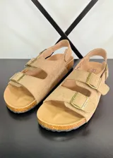 Sandalias planas color marrón claro con dos tiras anchas con hebillas y tira trasera.