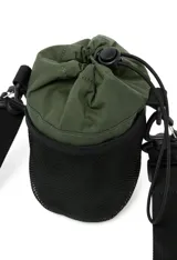 Bolsa tipo morral o porta botella de color verde oliva, con cierre de cordón ajustable en la parte superior y logo estampado en blanco en el frente. Cuenta con correas ajustables y ganchos de plástico negros para llevar cruzada o colgada.