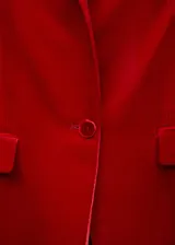 Blazer rojo de terciopelo con solapas de pico, cierre frontal con un botón, dos bolsillos delanteros de ribete con solapa y forro interior.