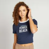 Camiseta azul marino de corte ajustado con cuello redondo blanco y estampado frontal con la frase "25 PARK ROAD STATION LA VENICE BEACH" en letras blancas.
