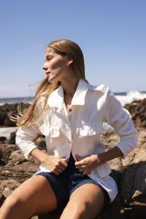 Chaqueta de denim liviana en color beige con detalle de volados en el frente, cuello camisero y bolsillos funcionales. Presenta un calce relajado y cierre frontal mediante botones.