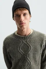 Sweater verde oliva de punto con cuello redondo, manga larga y diseño de trenzas en el frente.