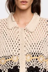 Cárdigan de algodón crochet color crema, con cuello camisero, manga corta y cierre frontal con botones. Presenta apliques de flores tejidas en negro y dorado. Corte oversize.