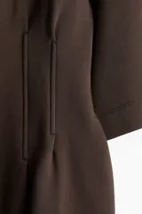 Remera larga marrón en punto pesado de algodón. Modelo con escote bote, hombros caídos y mangas amplias al codo. Cintura entallada con pinzas apenas acolchadas adelante y atrás.