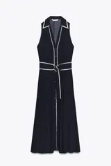 Vestido midi azul marino con estampado de lunares blancos, cuello solapa, escote en pico y sin mangas. Incluye cinturón de la misma tela y cierre frontal con botones.