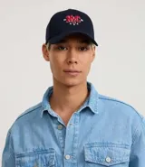 Gorra de sarga de algodón color marrón oscuro con visera curva y ajuste trasero. Presenta un bordado frontal con las letras 'NYC' en estilo universitario con detalles en rojo y blanco, flanqueadas por los números '19' y '86' y tres estrellas blancas debajo.