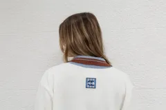 Buzo blanco de algodón con cuello polo con botones, mangas largas con puños acanalados a rayas en tonos marrón y celeste.