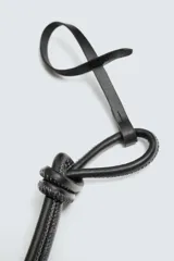 Llavero de cuero negro con detalle de nudo. El cordón presenta una ranura que permite ajustar el llavero como charm colgante en un bolso.