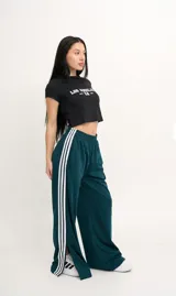 Pantalón de jogging verde oscuro con cintura elástica y tres rayas blancas verticales en los laterales.