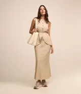 Conjunto color beige compuesto por una falda midi de lino y viscosa con lazo en la cintura y un chaleco sin mangas con botones. Incluye un bolso tote beige.