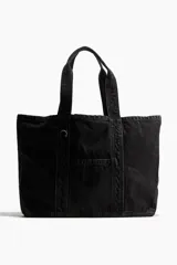 Bolso shopper grande de denim negro con efecto lavado. Tiene dos asas cortas, un bolsillo exterior abierto y un compartimento interior pequeño.