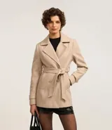 Saco color beige de polivelour, con cuello solapa, abotonado doble, bolsillos y cinturón para lazo.