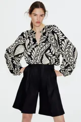 Blusa oversized de algodón y viscosa con estampado de hojas y lunares en blanco y negro. Tiene cuello mao, abertura frontal con botones forrados, mangas globo largas con puños abotonados y bajo redondeado.