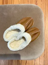 Pantuflas marrones de cuero lanar con interior de piel sintética blanca y suela de goma.