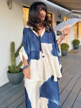 Camisa amplia de satén liviano con estampado floral rayado en tonos azul y blanco. Tiene cuello camisero, cierre frontal con botones y mangas 3/4. Ideal para usar abierta sobre un top o cerrada como prenda principal.