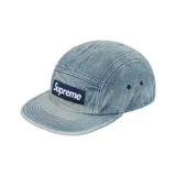 Gorra tipo camp cap de denim celeste lavado, con logo de Supreme en etiqueta rectangular azul marino en el frente.
