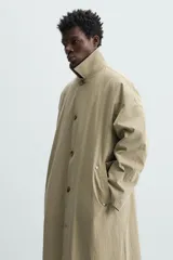 Gabardina color arena de corte amplio, con cuello solapa, manga larga, cierre frontal con botones y bolsillos laterales con solapa.