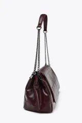 Bolso de hombro marrón oscuro de cuero sintético, con solapa y cierre magnético. Tiene un asa de cadena plateada y tres compartimentos internos, uno de ellos con cierre de cremallera.